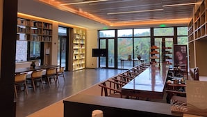 A modern library with bookshelves, a long wooden table, and a large window with a view of trees.