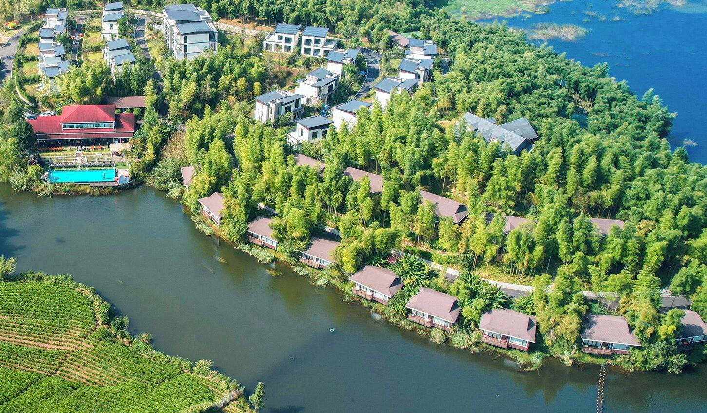 Vista aérea de un complejo turístico junto al lago, con varias edificaciones, una piscina y árboles densos alrededor.