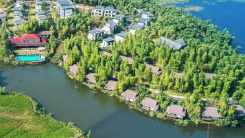 Vista aérea de un complejo turístico junto al lago, con varias edificaciones, una piscina y árboles densos alrededor.
