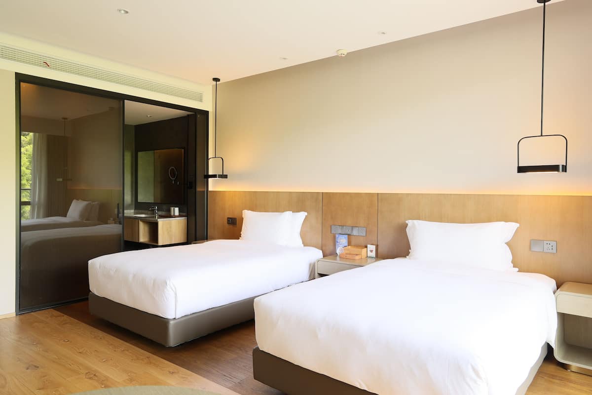 Una habitación de hotel moderna con dos camas, suelo de madera, un espejo grande y cabecero de madera.