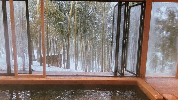 A wooden spa area with a view of a snowy forest through large windows.