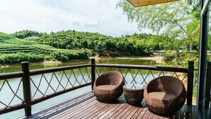 A wooden deck with wicker chairs overlooking a river and lush greenery.