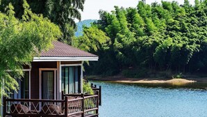 A wooden cabin with a balcony overlooking a lake, surrounded by dense forest.