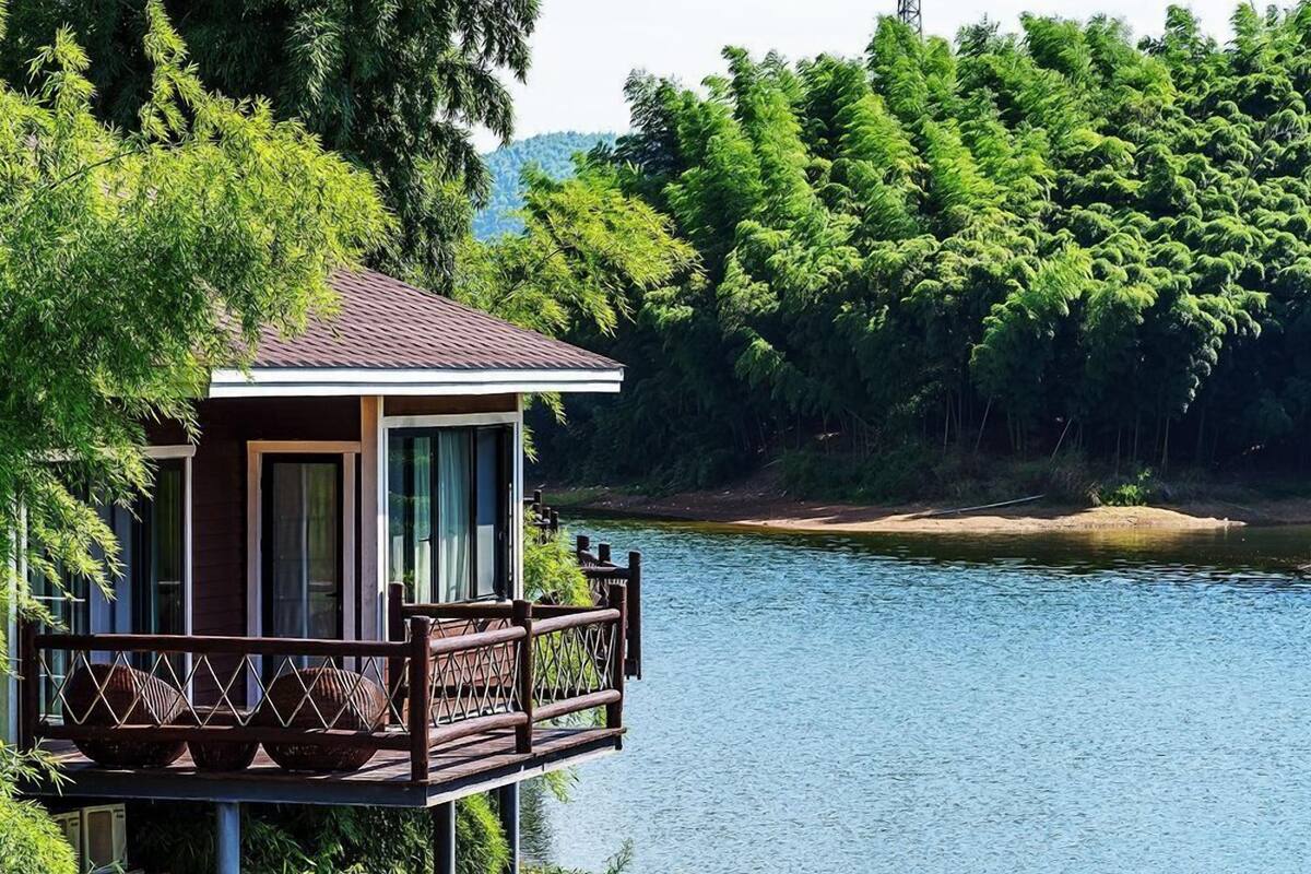 Una cabaña de madera con balcón que da a un lago, rodeada de un bosque denso.