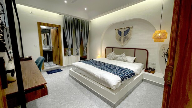 A modern bedroom with a large bed, a wooden desk, and a bathroom visible through an open door.
