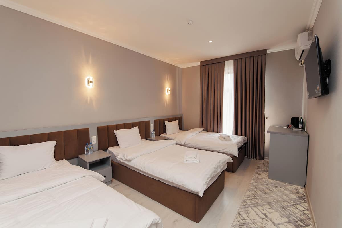 A hotel room with three beds, a desk, a TV, and a wall-mounted air conditioner.