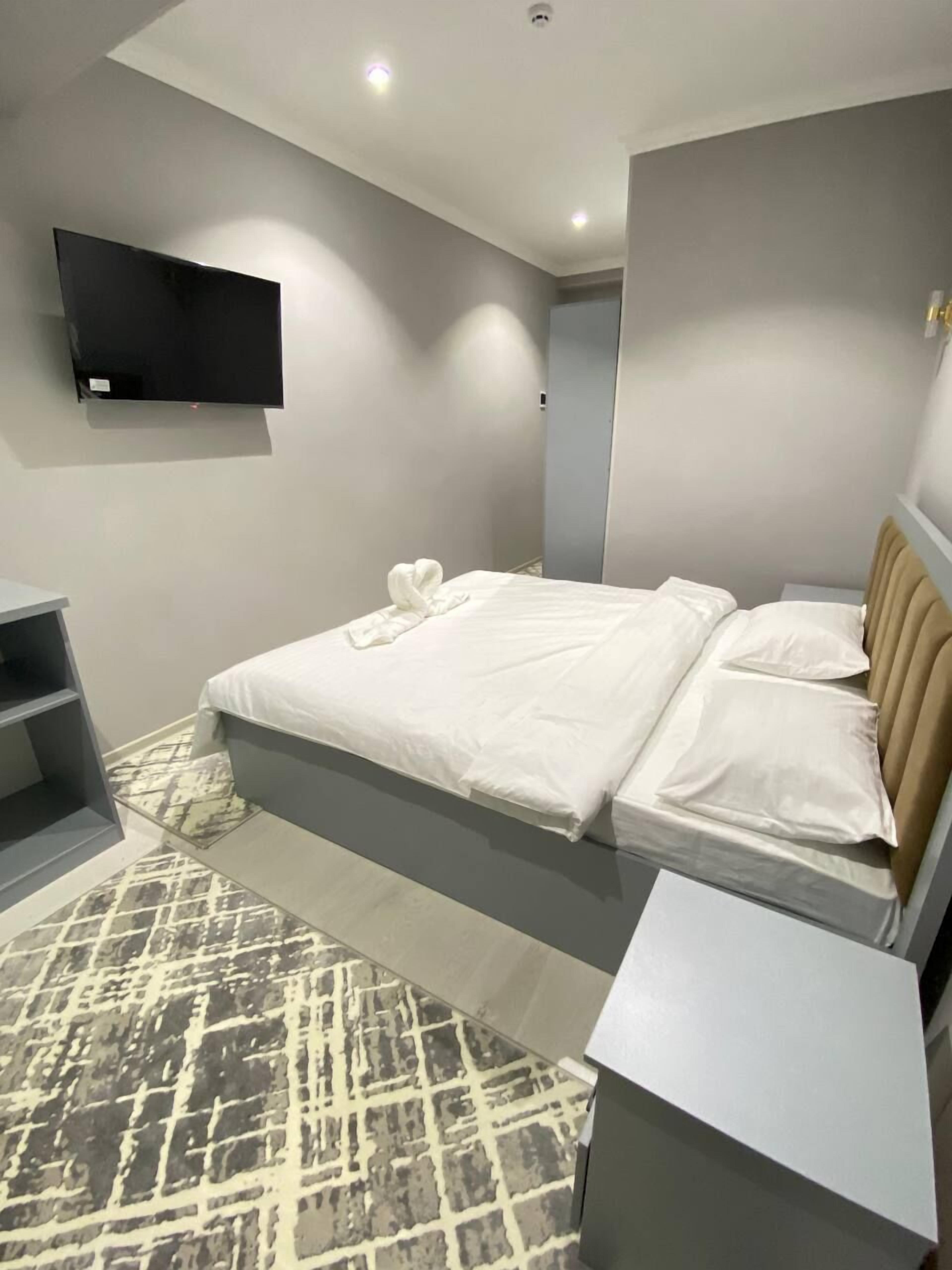 Una habitación de hotel moderna con una cama grande, un televisor de pantalla plana montado en la pared y una mesita de noche pequeña.
