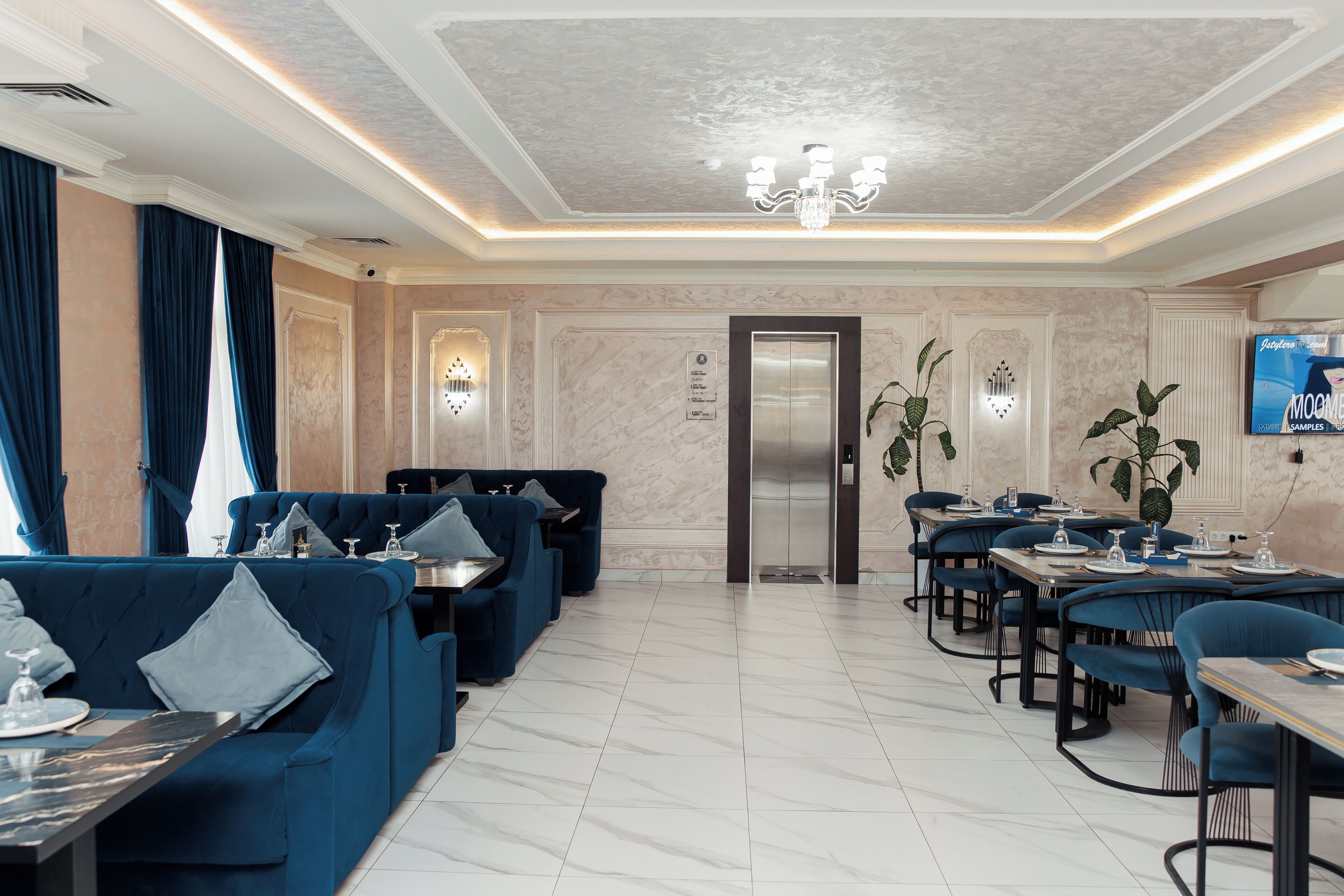 A modern dining area with blue upholstered seating, marble flooring, and a chandelier.