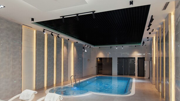 A modern indoor swimming pool with a glass table and wicker chairs in the foreground. - Polar Bear (Samarkand)