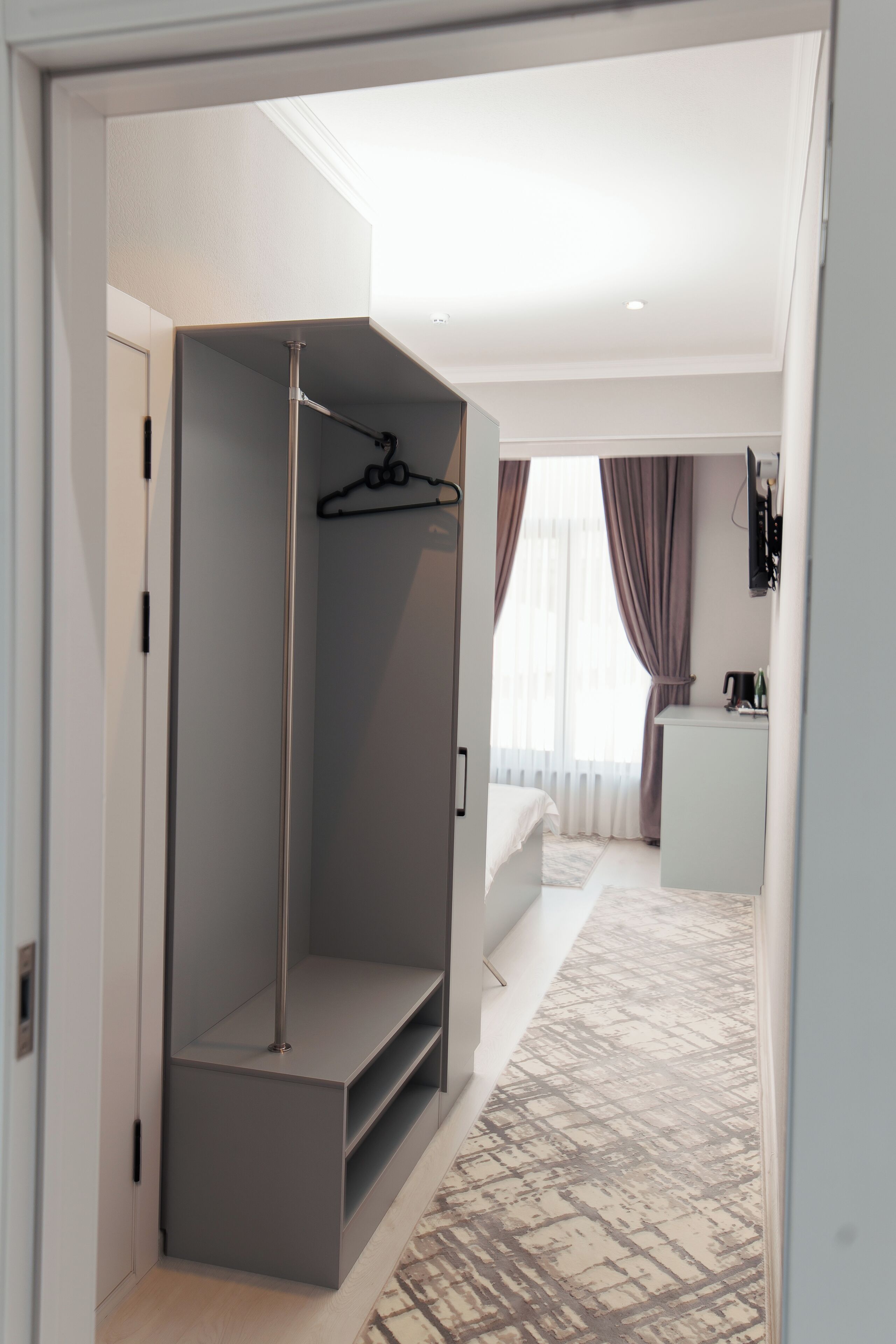 A modern hotel room with a walk-in closet, a bed, a desk, and a bathroom.