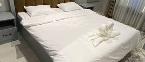 Une chambre d’hôtel avec un grand lit, une table de chevet, une commode et une fenêtre avec des rideaux.