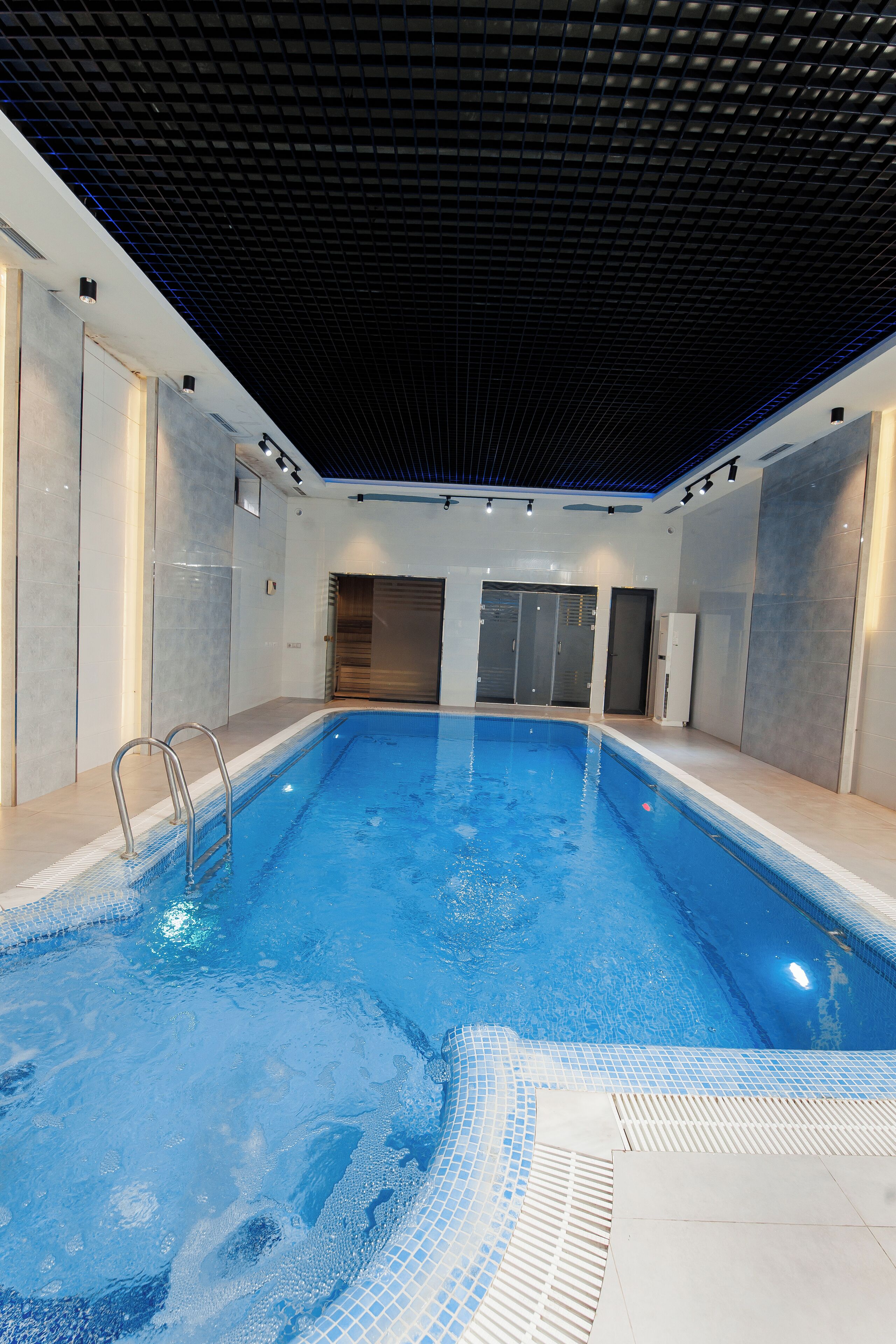 An indoor swimming pool with clear water, tiled walls, and a ceiling with a grid pattern.