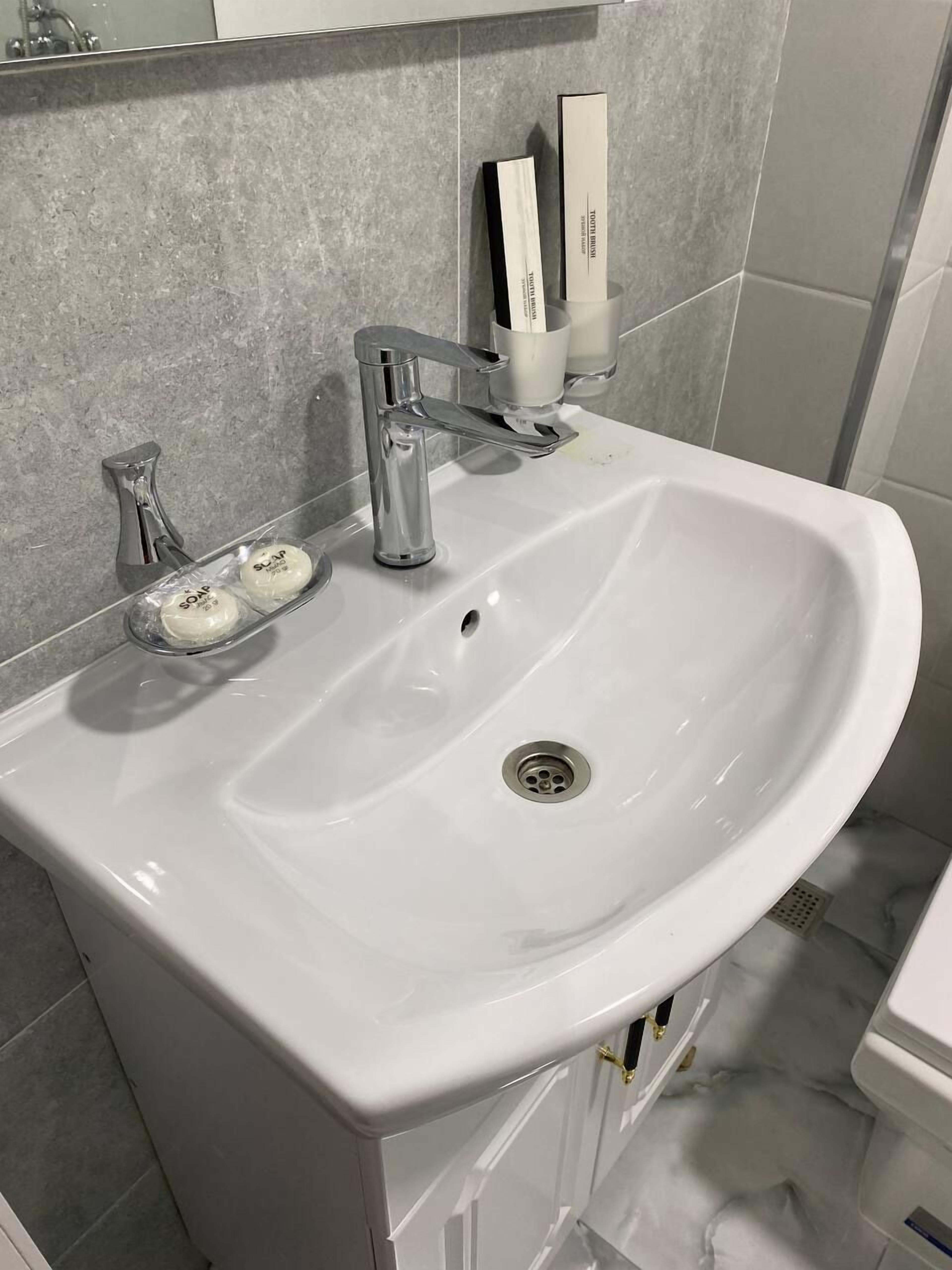 A white bathroom sink with a modern faucet, soap dispensers, and a soap bar.
