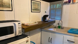 A compact kitchenette with a microwave, a small refrigerator, a sink, and a window with blinds. - Alemão Cabanas (São Sebastião)