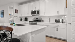 Cocina moderna con armarios blancos, electrodomésticos de acero inoxidable y una isla central.