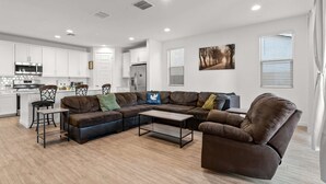 Una sala moderna con un sofá seccional, una mesa de centro y un comedor con una cocina al fondo.