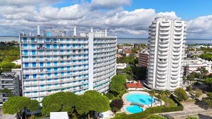A high-rise hotel with multiple balconies, a swimming pool, and a view of the sea. - Spacious apartment near beach with pool (Lignano Sabbiadoro)