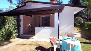 Un pequeño espacio exterior techado con una mesa y sillas, una ventana con mosquitero y una pared de ladrillo.