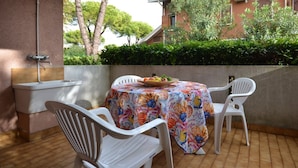 An outdoor patio with a table covered in a colorful tablecloth, surrounded by white plastic chairs.