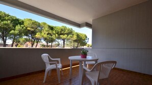 A balcony with a tiled floor, white plastic chairs, a small round table with a potted plant, and a view of trees and buildings. - Centric studio flat with terrace (Bibione)