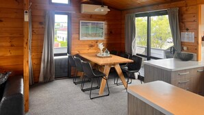 L’intérieur d’un chalet en bois comprend une table à manger, des chaises, un coin cuisine et de grandes fenêtres.