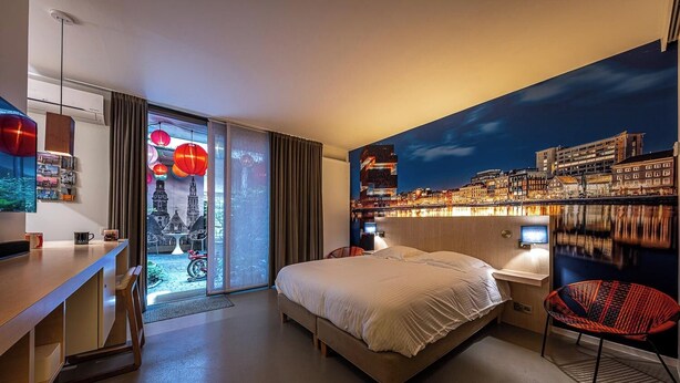 A modern hotel room with a large bed, a desk, a chair, and a cityscape mural on the wall. - Antwerp For Two B&B for value seekers (Antwerpen)