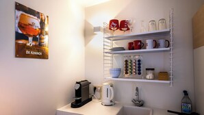 A kitchen with a coffee maker, a kettle, a sink, and shelves holding mugs and a muffin tin. - Antwerp For Two B&B for value seekers (Antwerpen)