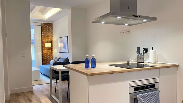 A modern kitchen with a central island, built-in oven, and a stainless steel range hood. - w* | Majestic 2BR at Palacio Real (Madrid)