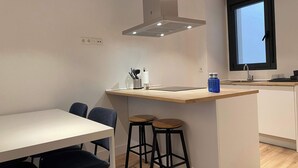 A modern kitchen with a central island, bar stools, a dining table, and a window. - w* | Majestic 2BR at Palacio Real (Madrid)