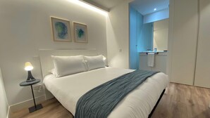 A modern bedroom with a large bed, a bedside lamp, and a bathroom visible through an open door. - w* | Majestic 2BR at Palacio Real (Madrid)