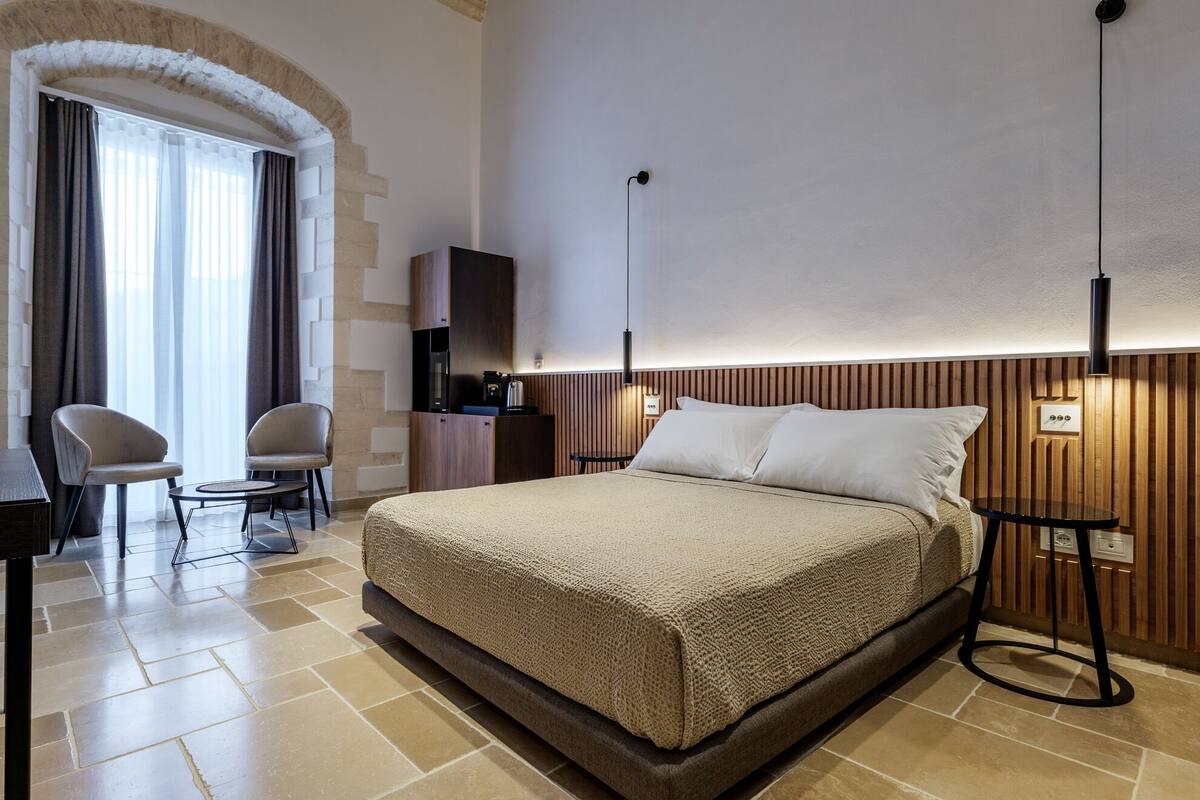 Une chambre d’hôtel avec un grand lit, un bureau avec des chaises, une télévision et un luminaire fixé au mur.