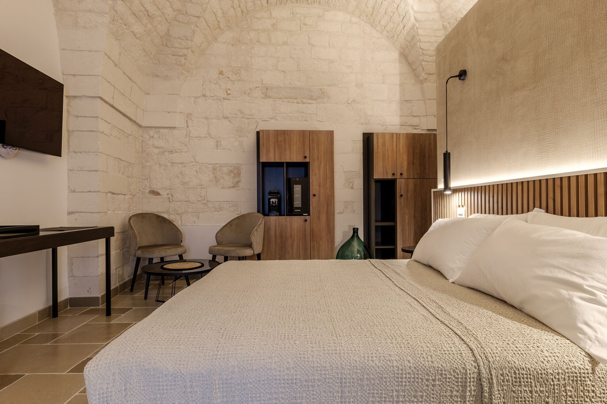 Un dormitorio con una cama grande, un televisor montado en la pared, un armario de madera y dos sillas.