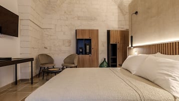 Un dormitorio con una cama grande, un televisor montado en la pared, un armario de madera y dos sillas.