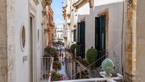 A narrow street with buildings on either side, balconies with green shutters, and a pedestrian walkway. - buone maniere exclusive room (Martina Franca)