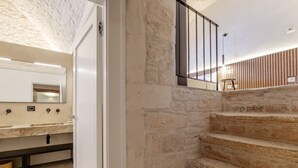 A bathroom with a marble countertop, a large mirror, and a stone wall. - buone maniere exclusive room (Martina Franca)