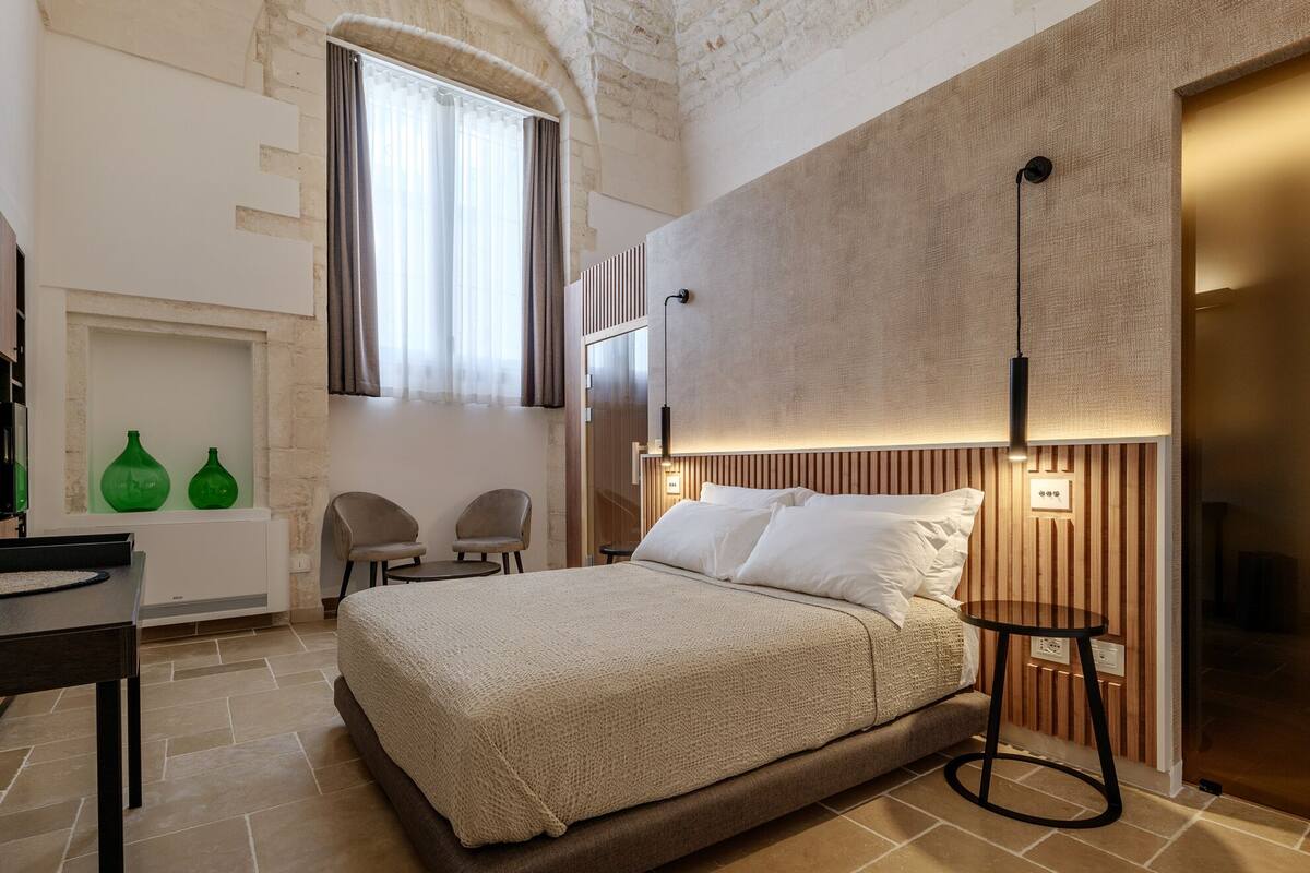 Une chambre moderne avec un grand lit, deux fauteuils, une petite table et une fenêtre avec des rideaux.