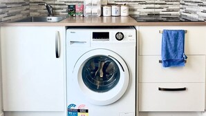 A compact laundry room with a front-loading washer and dryer, a microwave, and a tiled backsplash. - Your separate space in Wigram. (Christchurch)