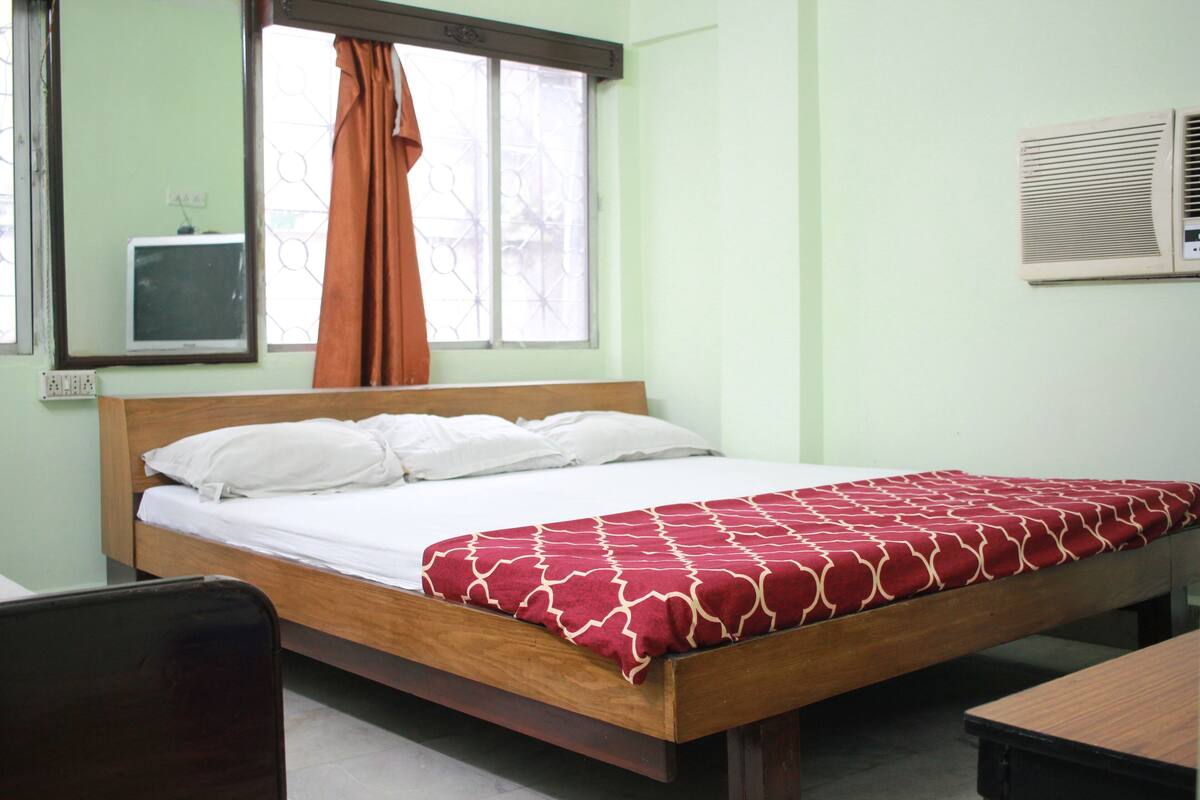 A single-bed room with a wooden frame, white bedding, and a red patterned bedspread.