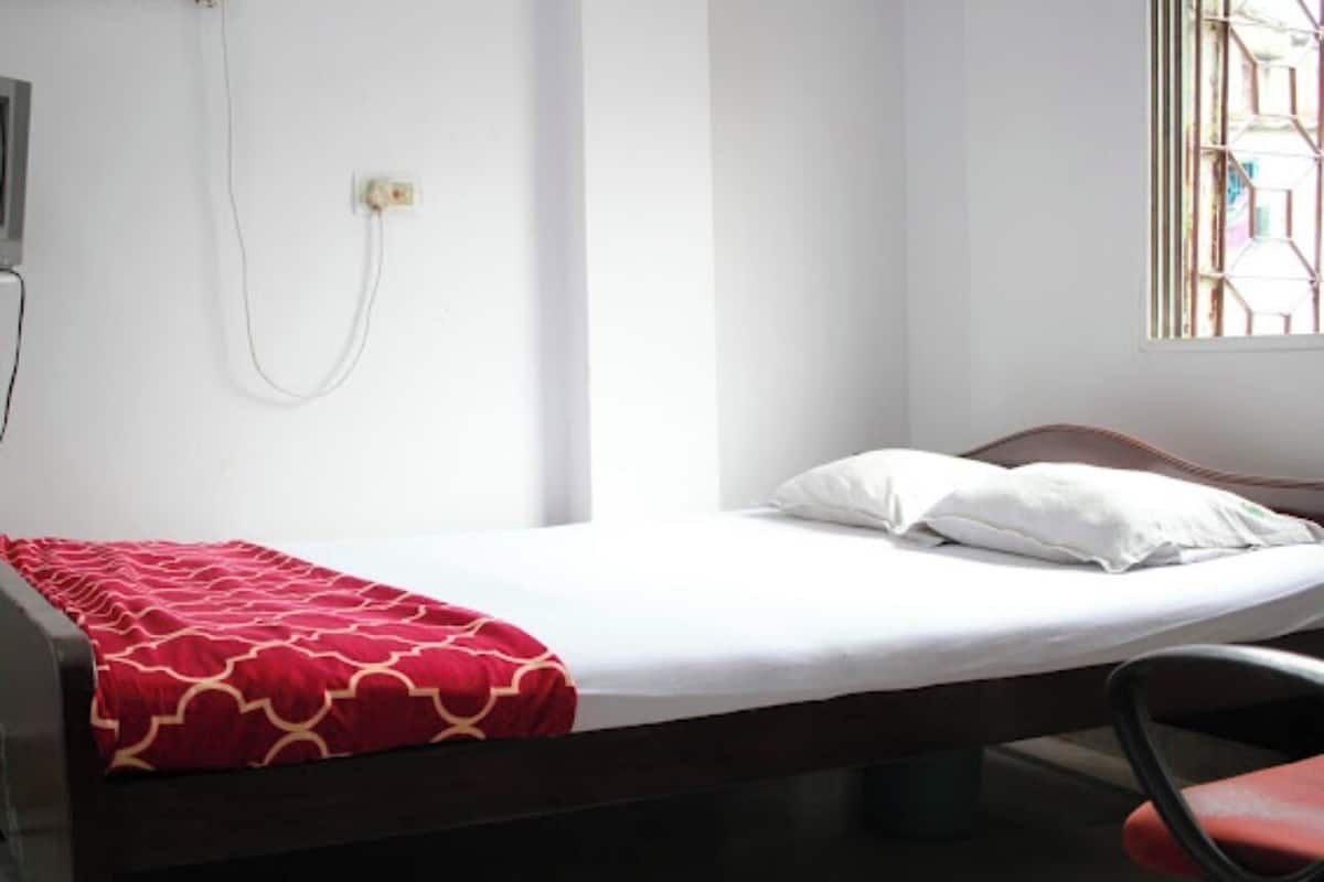A single bed with a red patterned bedspread, a white pillow, and a wooden headboard.