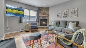 A living room with a fireplace, a large flat-screen TV, a gray sofa, and a patterned rug.