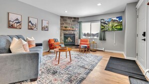 A living room with a stone fireplace, a large TV, and a sofa. - Ellicottville 2 miles to Holiday Valley Condo 4 (Great Valley)