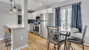 A modern kitchen with white cabinets, stainless steel appliances, and a marble island with bar stools. - Ellicottville 2 miles to Holiday Valley Condo 4 (Great Valley)