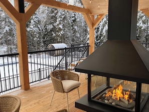 Un porche cubierto con chimenea, sillas de mimbre y vistas a árboles nevados.