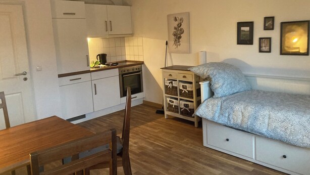 Una cocina compacta con armarios blancos, una mesa de comedor de madera y un sofá con ropa de cama estampada.