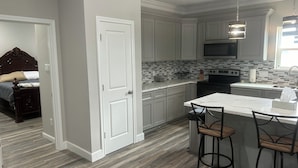 A modern kitchen with white cabinets, a tiled backsplash, a stainless steel sink, and a bar area with stools.
