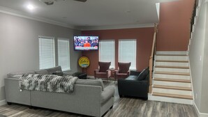 A living room with a gray sectional sofa, two armchairs, a TV, and a staircase.