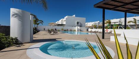 A modern pool area with a circular hot tub, lounge chairs, and a covered seating area.