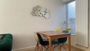 En matplats med ett träbord och stolar, en grön soffa och en spegel som hänger på väggen.