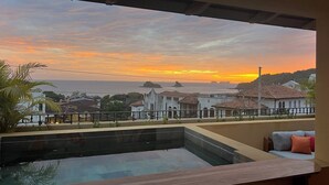 A pool area with a view of a coastal town at sunset.