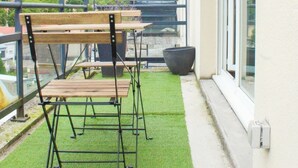 A balcony with a wooden table and chairs, a potted plant, and a view of the cityscape. - The SkyFall: superb apartment, terrace and parking space (Longwy)